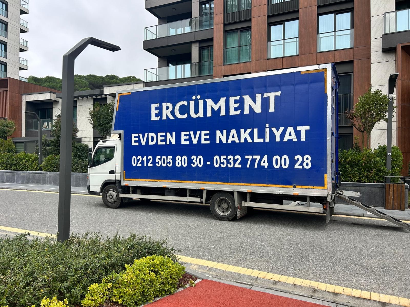 Rampası açık Ercüment Nakliyat kapalı kasa kamyonu bir binanın önünde